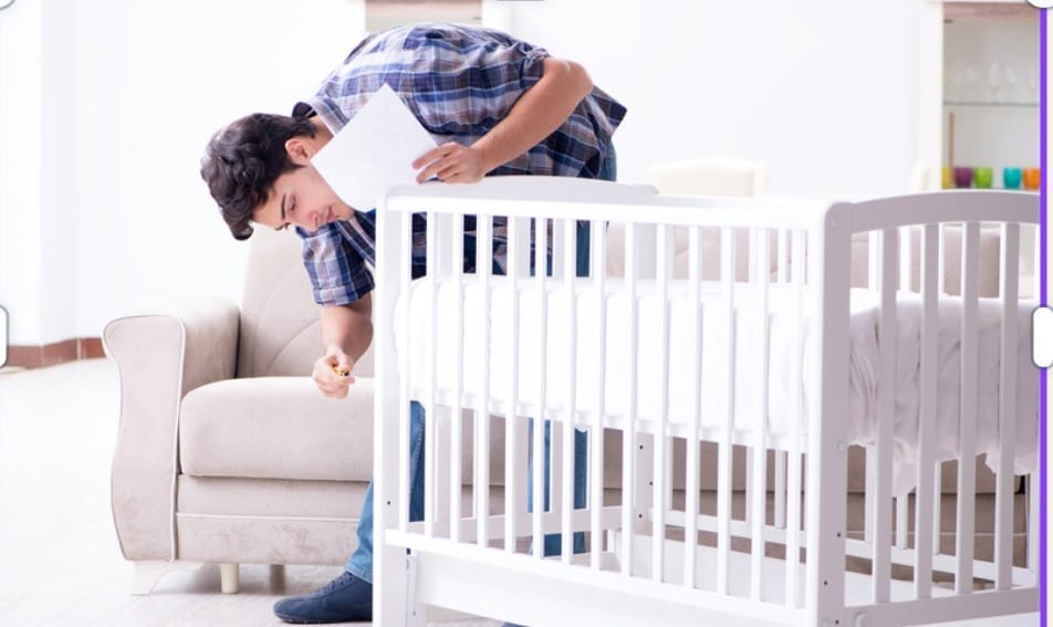 Un parent monte un lit de bébé en suivant la notice, dans le salon